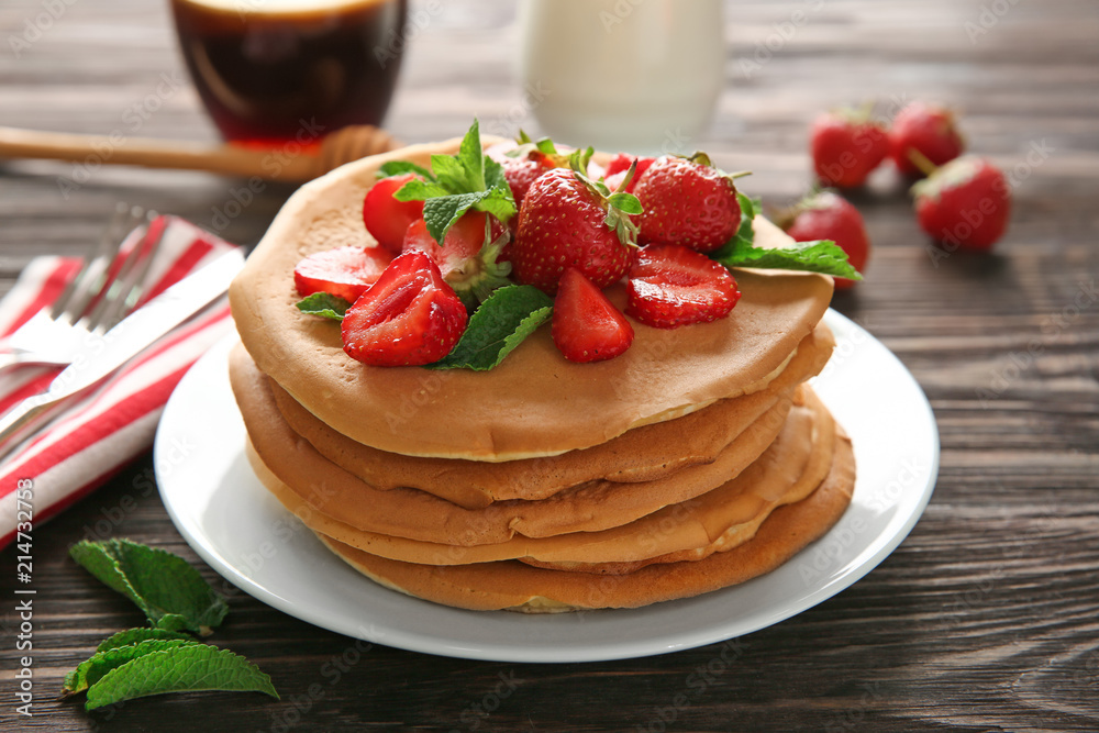 Plate with delicious pancakes and strawberries on wooden table