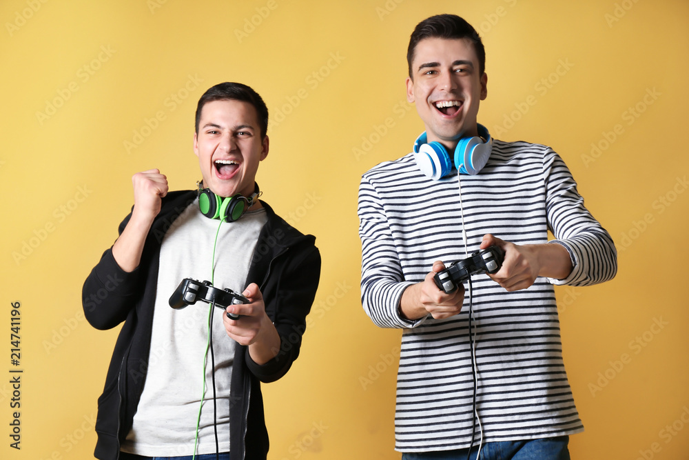 Young men with gamepads on color background