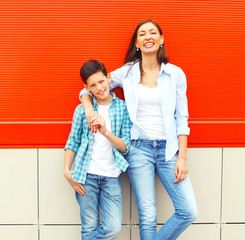 Fashion smiling mother with son teenager together on red background