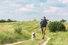 Traveler Running With Dog On Path On Summer Meadow