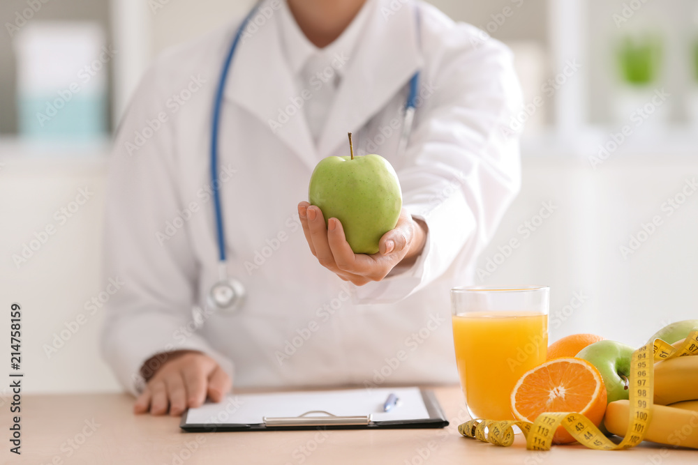 Female nutritionist with fresh apple sitting at table in her office