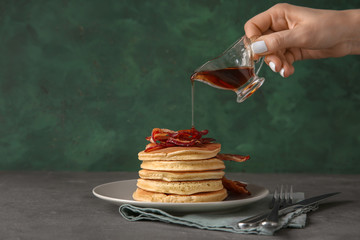 woman pouring maple syrup onto tasty pancakes with fried bacon