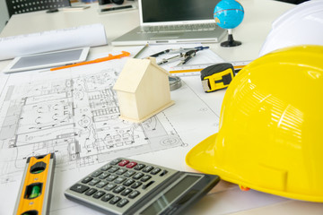 Architecture Desk with equipment architects On the desk with blueprint plan, helmet, wooden house model and tools in the engineering office room. Selective Focus.