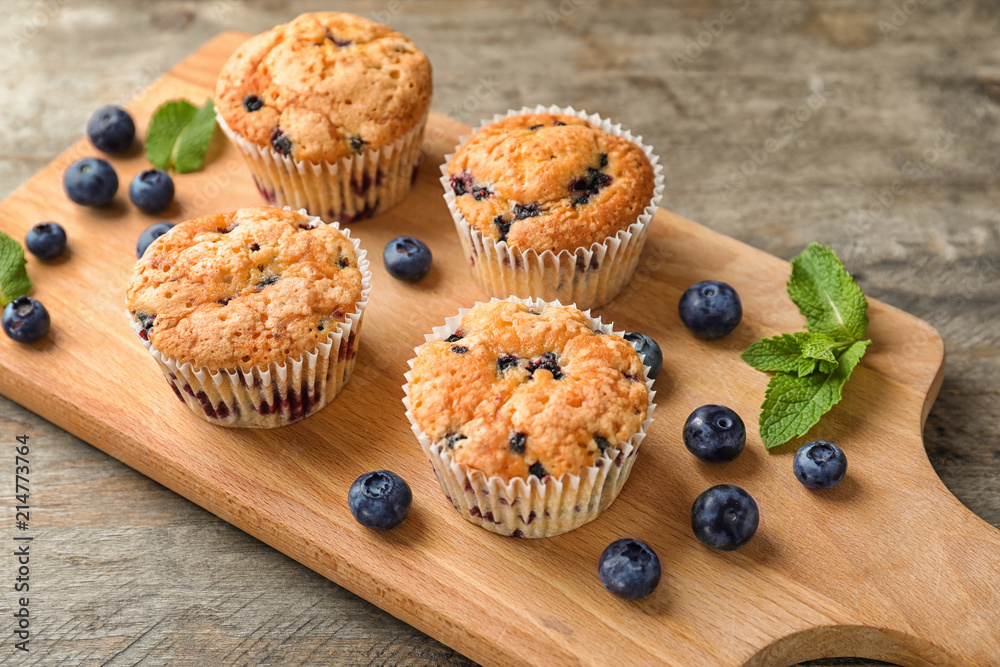 Wooden board with tasty blueberry muffins on table