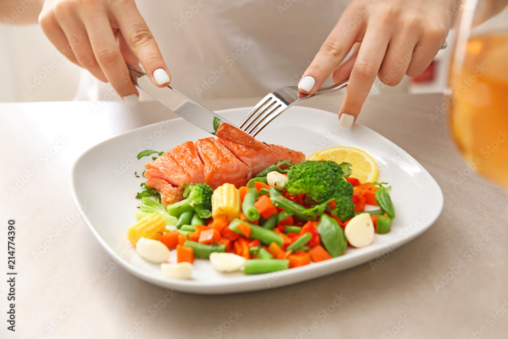 Woman eating fresh salad and fish at light table