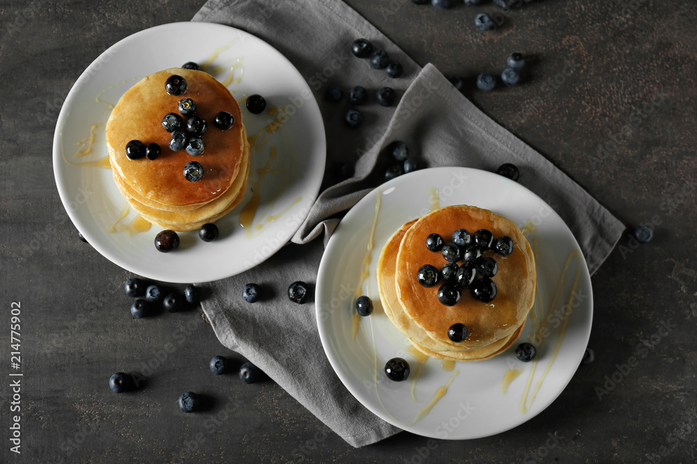 Plates with delicious pancakes and berries on dark table