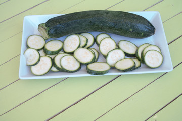 zucchini in a white tray on a green wooden table seen close up