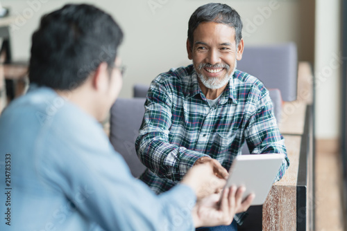 Fotomural Happy old short beard asian man sitting, smiling and listen to partner that showing presentation on smart digital tablet