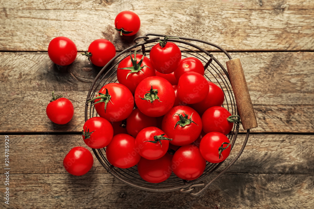 Metal basket with fresh cherry tomatoes on wooden background