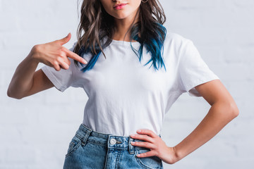 cropped image of young woman pointing by finger on empty white t-shirt