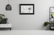 Poster on grey wall in empty living room interior with plants, lamp and cupboard. Place for your sofa. Real photo