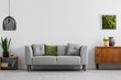 © Photographee.eu - Grey sofa with pillows next to wooden cupboard in living room interior with lamp and poster. Real photo
