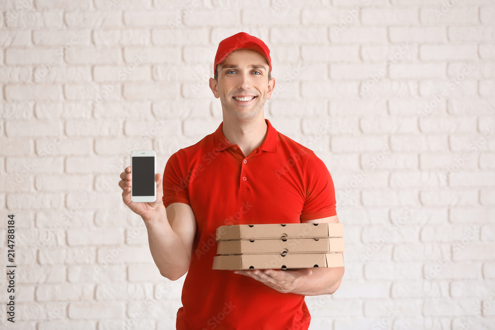 Young man with pizza boxes and mobile phone near white brick wall. Food delivery service