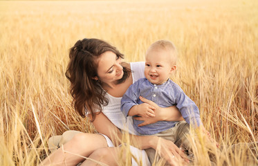 Beautiful woman with her little son in wheat field on summer day