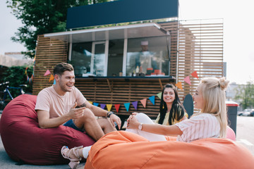 Poster - happy young friends talking while sitting on bean bag chairs near food truck