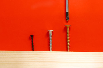 screwdriver, screws and wood close-up on a red background