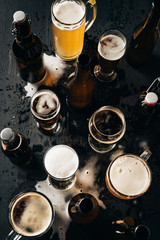 Wall Mural - top view of arrangement of bottles and glasses of beer on dark wooden tabletop