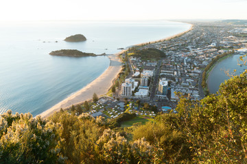 Canvas Print - Mount Maunganui stretches out below as sun rises on horizon and falls across ocean beach and buildings