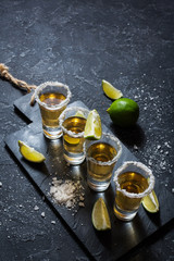 Wall Mural - Mexican gold tequila with lime and salt on black stone background.