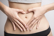 © mkphoto2000 - Close-up of a slim woman with a thin waist in black panties and gray short top making a heart with her hands on stomach.