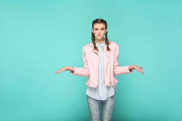 confused doubtful portrait of beautiful cute girl standing with makeup and brown pigtail hairstyle in striped light blue shirt pink jacket. indoor, studio shot isolated on blue or green background.