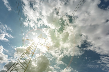 Silhouette of the high voltage electric pylon towers on the background of beautiful clouds with sun rays