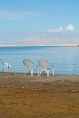 Two white plastic chairs on lowest salty lake in world below sea level Dead sea, Israel, near Ein Bokek, perfect place for medical treatments, climatotherapy, thalassotherapy and heliotherapy.