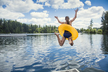 A Little Girl Jumping Off The Dock Into A Beautiful Mountain Lake. Having Fun On A Summer Vacation