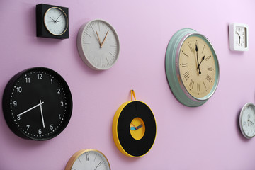 Many different clocks hanging on color wall. Time of day