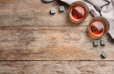 Glasses with liquor and whiskey stones on wooden background, top view