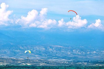 Wall Mural - Two Paraglider flies. paraglider over the  mountains,city in summer sunny day.