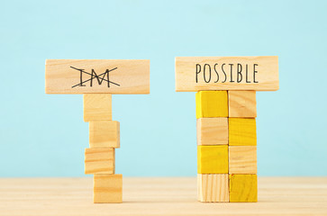 Poster - concept image of Wooden cubes that create an unstable structure and the word im next to steady one with the word possible.