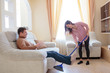 © Aleksei Lazukov - Happy woman cleaning floor with mop while man sitting on sofa