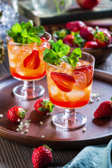 Wall Mural - Red cocktail with ice, mint leaves and strawberry on wooden background.