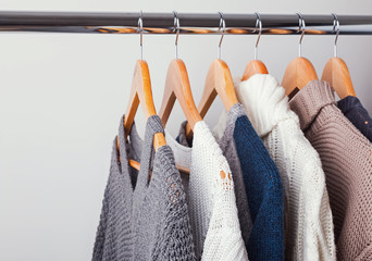 Different knitted sweaters on hangers close-up