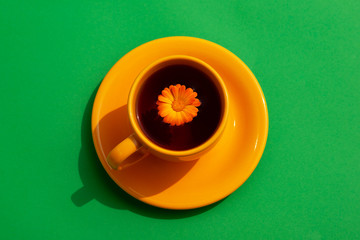 Wall Mural - Yellow tea cup on a green background. Tea with a flower in spring and summer style. A cup of tea under the summer sun.