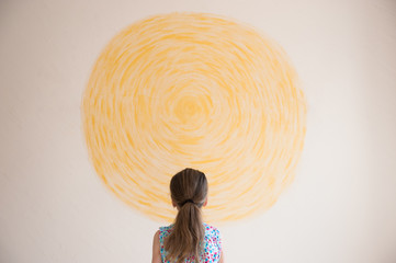 little caucasian girl looking at yellow sun painted on wall indoors