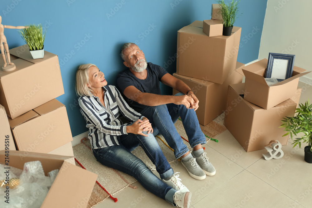 Mature couple sitting on floor near boxes indoors. Moving into new house