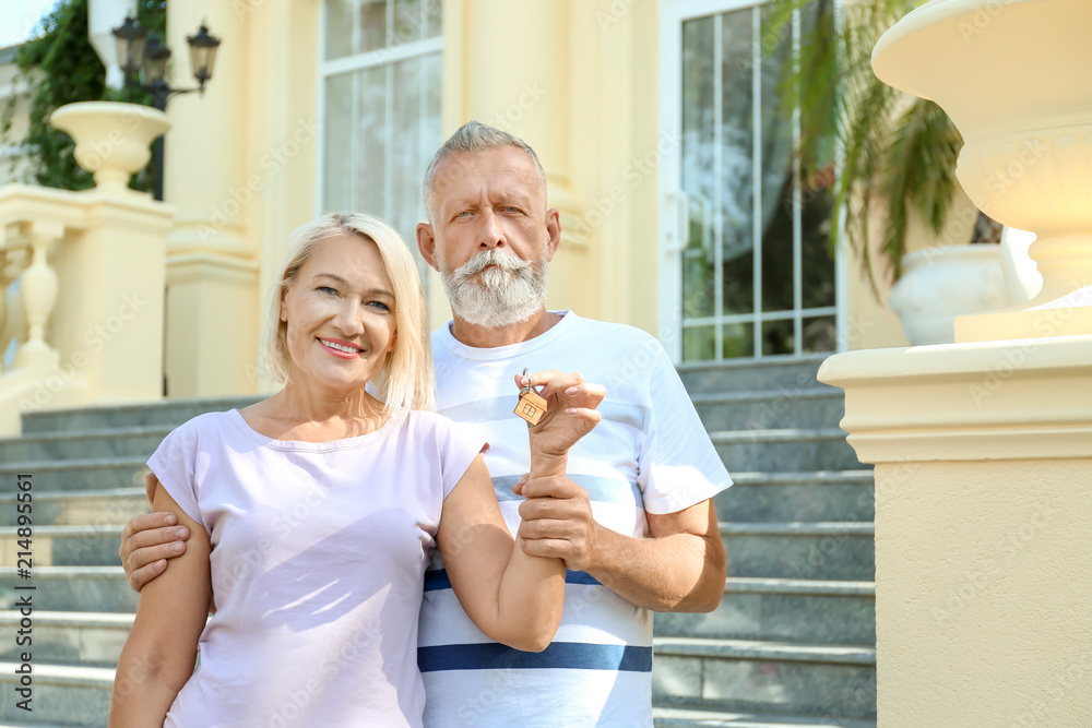 Happy mature couple with key outdoors. Moving into new house