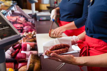 Sales women in butcher shop selling meat and sausages, close-up