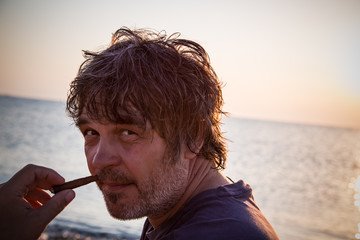 A man with a cigar looking at camera / Portrait of good looking middle aged man on the beach while sunsets