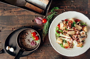 meat salad with bacon, cheese, vegetables and croutons at dark wood table