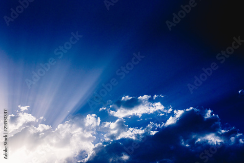 Photographie Sunbeams rising from a large cloud in intense blue sky on a summer afternoon