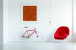 © Photographee.eu - Red bicycle next to armchair in minimal white apartment interior with painting and lamp. Real photo