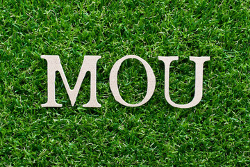 Wall Mural - Wood alphabet in word MOU (abbreviation of memorandum of understanding)on artificial green grass background