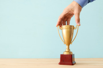 image of businessman holding a golden trophy over wooden table.