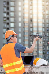 Wall Mural - Young Asian engineer man working with drone laptop and smartphone at construction site. Using unmanned aerial vehicle (UAV) for land and building site survey in civil engineering project.