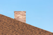 Red brick chimney on shingle roof od new modern house under blue sky on sunny day in summer