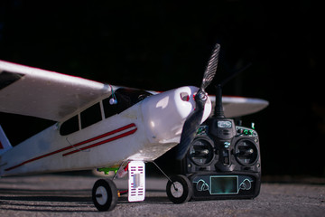  RC airplane in white with black propeller and a transmitter after landing on the street with concrete