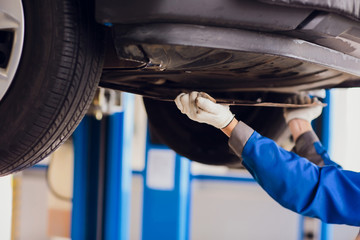 Young mechanic fixing wheel under car in service